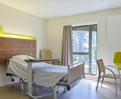 Chambre simple avec lit médicalisé, grande fenêtre et bureau